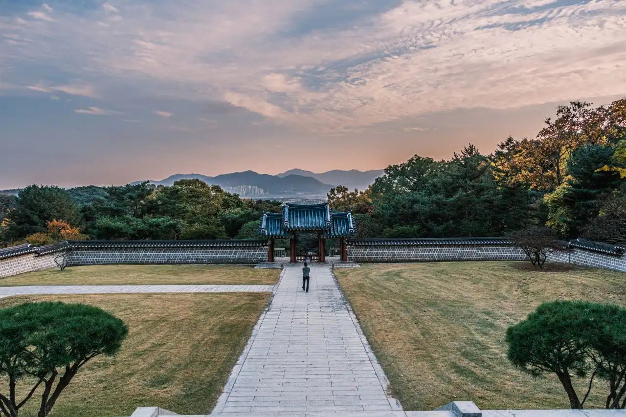 A blue-tiled gate and stone wall at the end of a paved path, with distant hills under a dusk sky