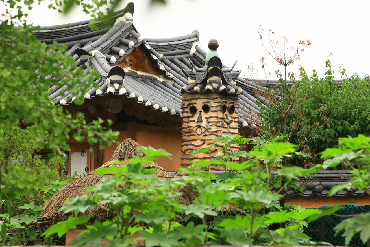 A tiled roof and a clay chimney patterned like a face, seen through green leaves