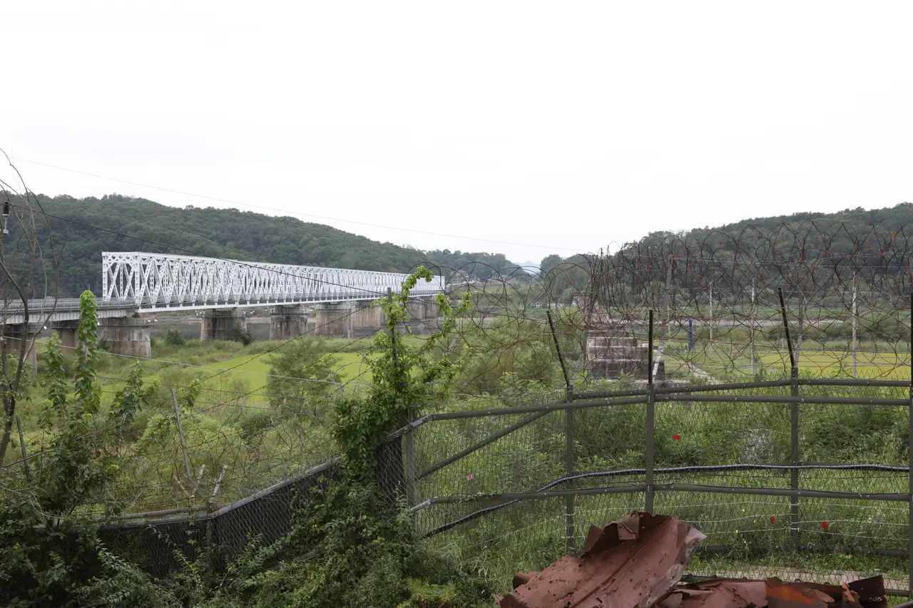 A white railway bridge seen past rusted barbed-wire fencing along the Imjin River
