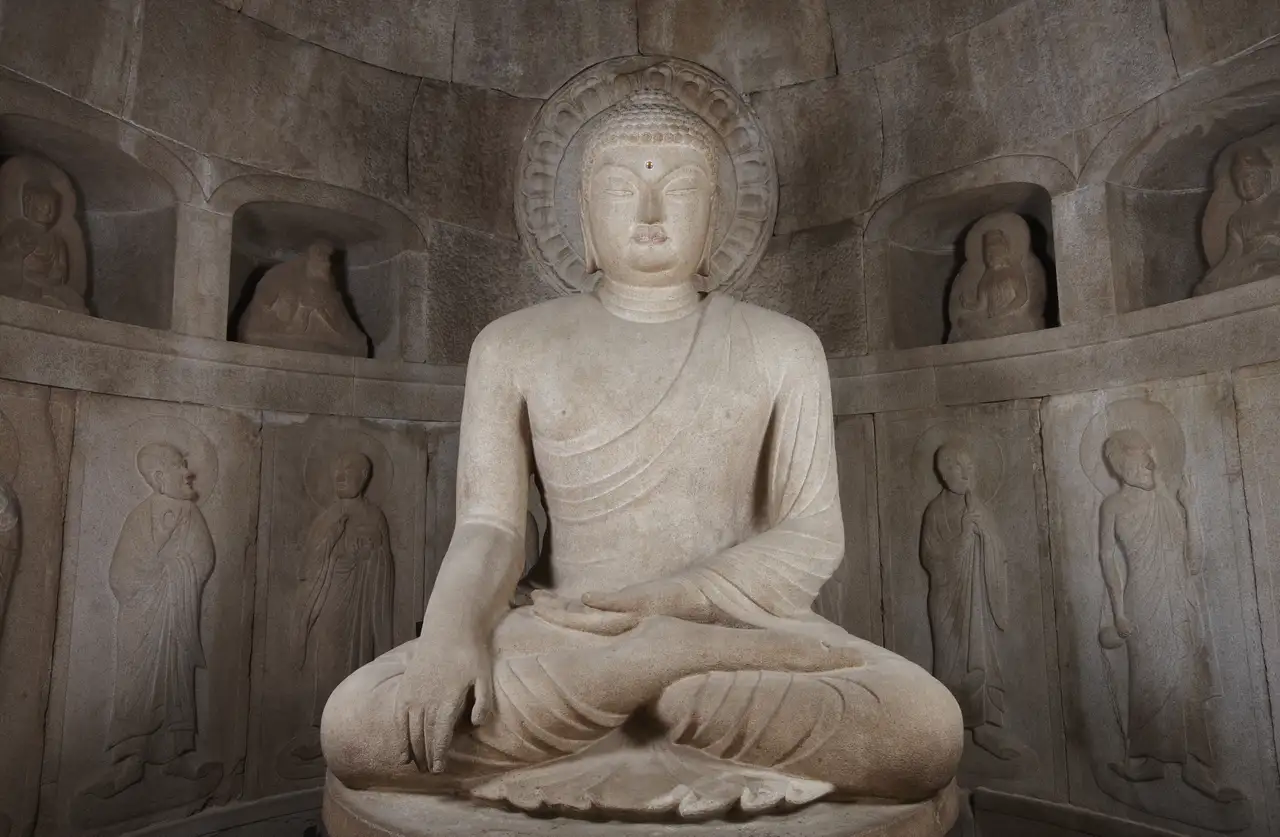 The granite main Buddha seated cross-legged before its round halo, niches of bodhisattvas and reliefs of disciples on the curved wall behind