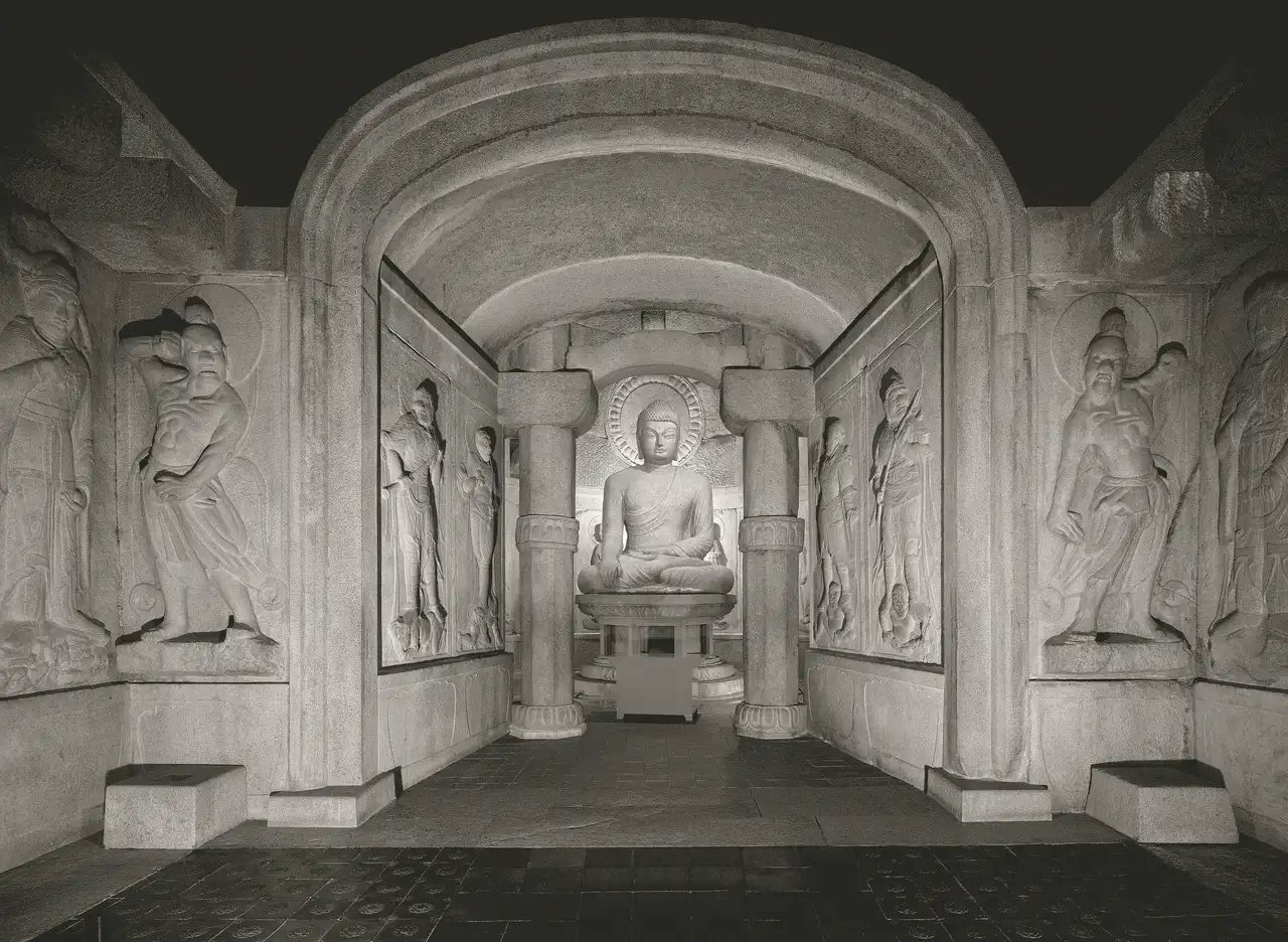 Black-and-white view from the front chamber: guardian reliefs line the walls of the arched passage leading to the main Buddha in the round chamber