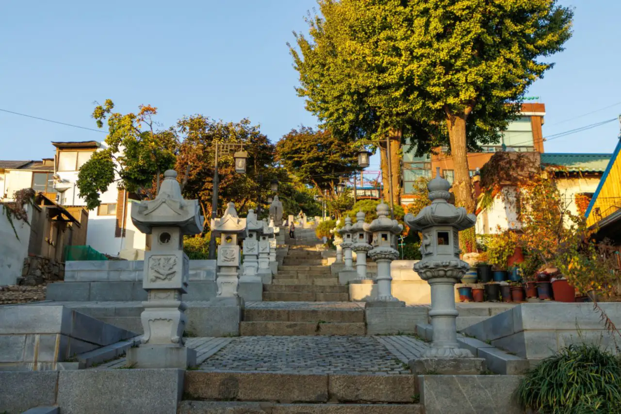 Stone steps flanked by rows of stone lanterns climbing toward trees on the hill