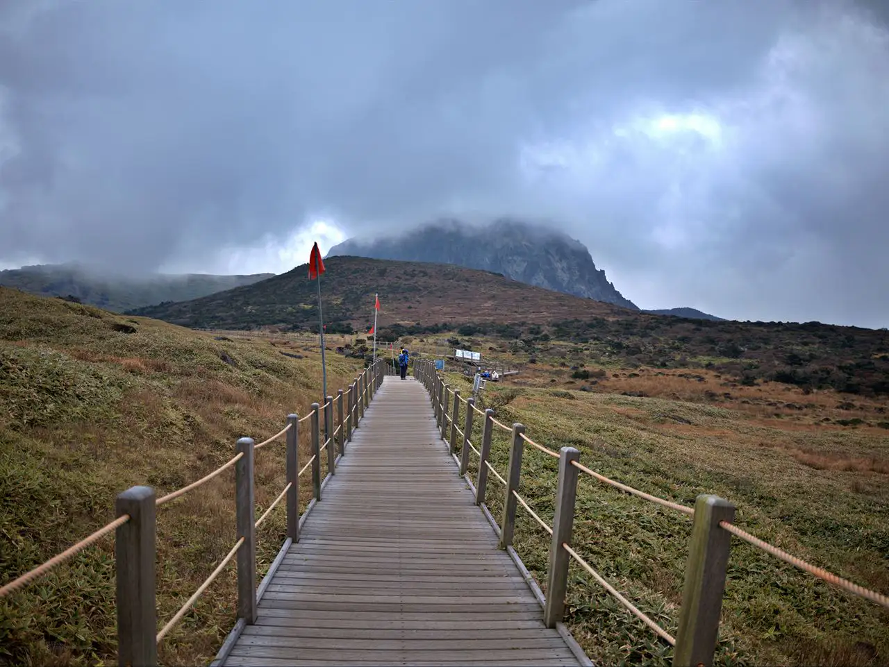 A straight wooden boardwalk across the autumn highland toward the cloud-capped peak (Yeongsil trail)