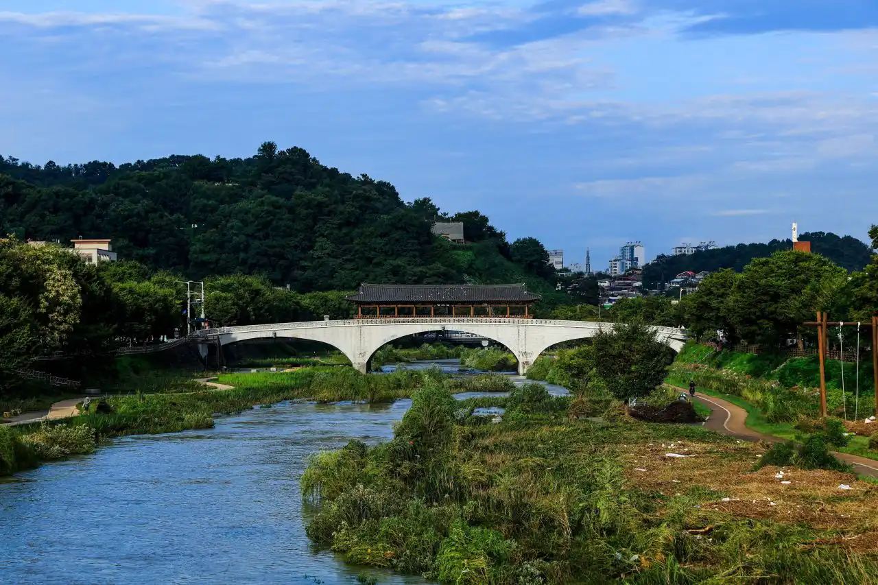 The Jeonjucheon stream running past the hanok village, an arched stone bridge with a pavilion and hills beyond