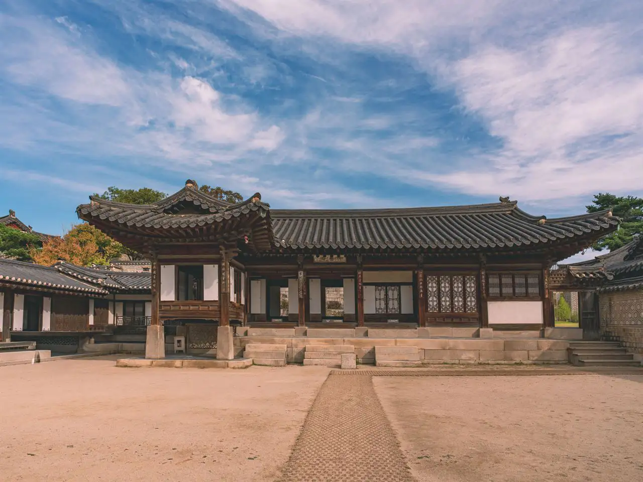 A Changdeokgung hall and its walls beyond an earthen courtyard under an autumn sky