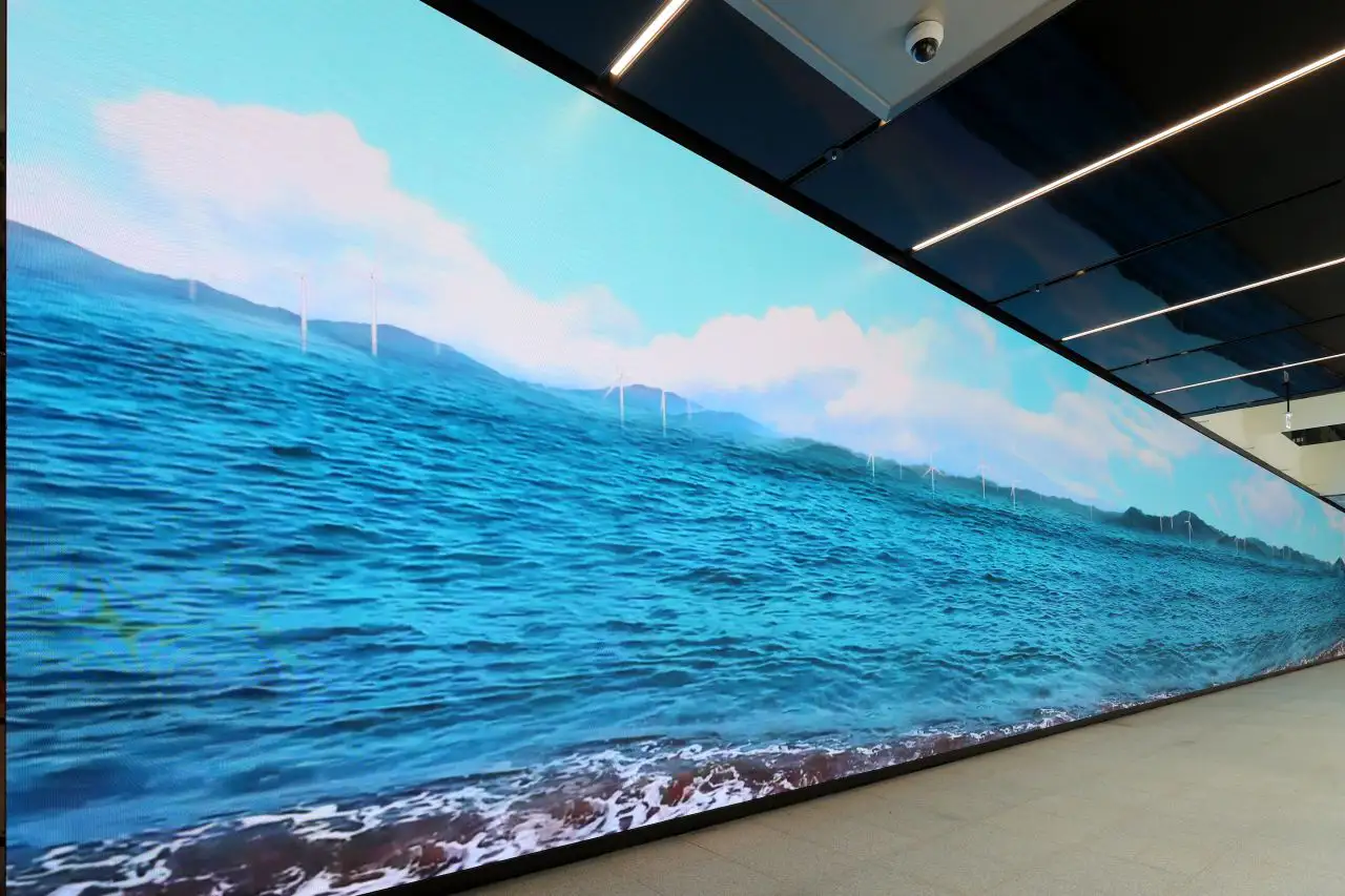 The long first-floor media wall filling a whole side of the hall, showing a sea with wind turbines
