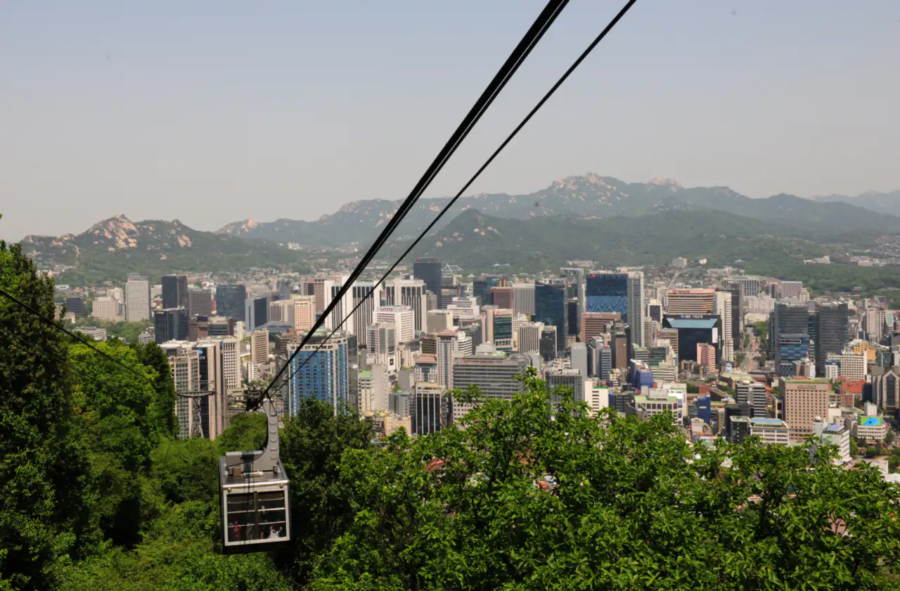 The Namsan cable car over the trees, with downtown Seoul and mountains behind
